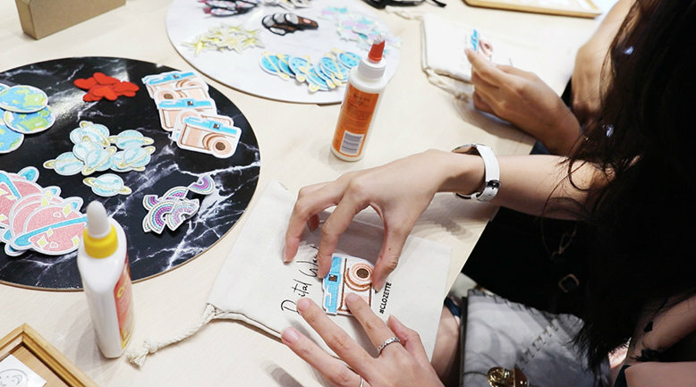 Pouch customisation A woman customising her small canvas pouch with various designs.