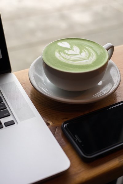 Matcha in a white ceramic cup beside a laptop