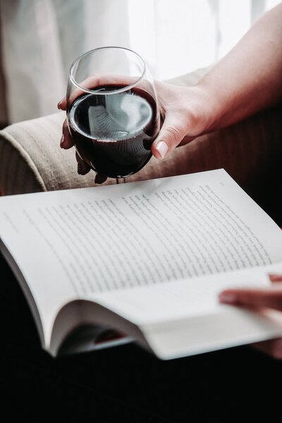 Person holding glass of red wine while reading a book