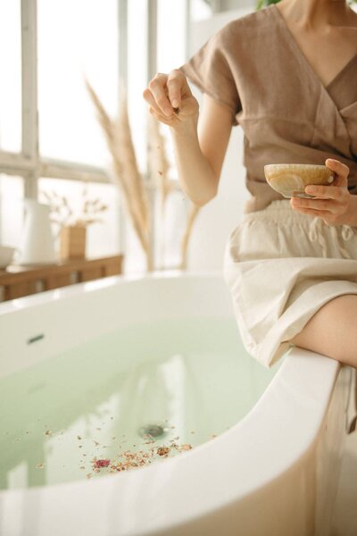 Woman sitting beside bathtub and putting bath salts