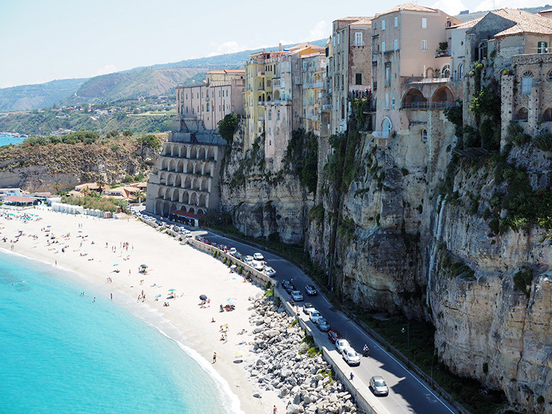 A view of a beach-side with an overlooking cliff full of houses