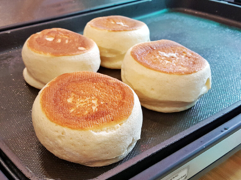 Four Japanese pancakes being fried on a hot skillet