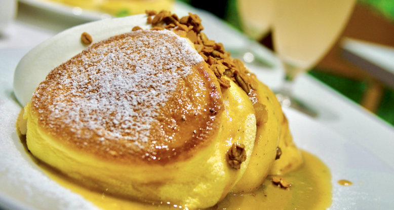 A stack of fluffy Japanese Soufflé pancakes with syrup and a dusting of sugar