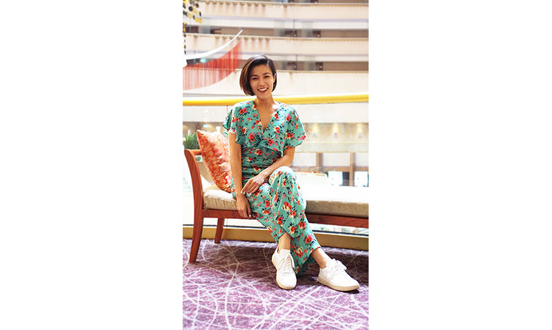 Woman sitting on a chair wearing blue floral printed jumpsuit and white sneakers