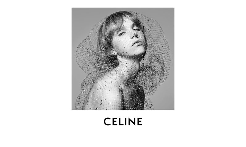 A woman covered with a net-like veil poses above CELINE's new logo