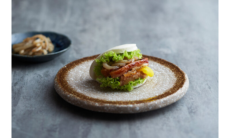 Braised kurobuta pork belly enveloped by a steamed bun, placed on a stone plate.