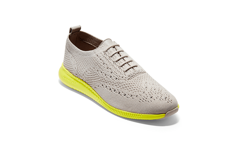 A grey knitted wingtip oxford shoe with neon green rubber outsole.